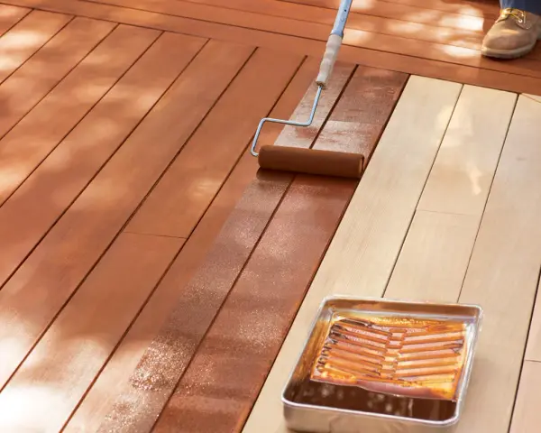 Aplicando protector para proteger madera exterior. Un rodillo extiende el líquido sobre las tablas de madera de una terraza.