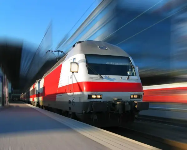 Pędzący pociąg PKP z czerwonym pasem na białej lokomotywie, na tle rozmytego nieba i torów.