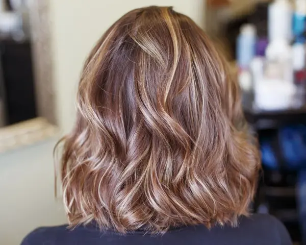 Piękne, falowane włosy z subtelnymi refleksami blond, które dodają im głębi i blasku.