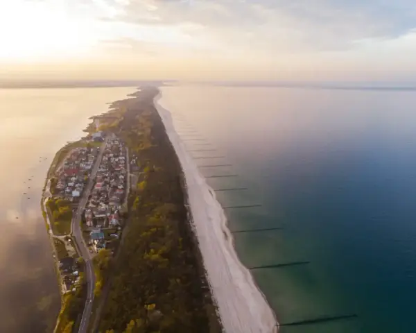Widok z lotu ptaka na malownicze chałupy nad morzem, z piaszczystą plażą i spokojną wodą.