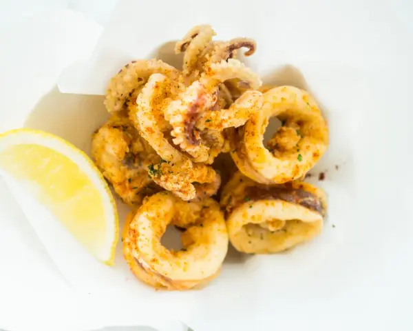 Crujientes calamares a la andaluza, dorados y sazonados, servidos con una rodaja de limón fresco.
