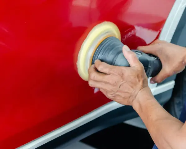 Ręce polerują czerwony lakier auta maszyną polerską. To kluczowy etap, jak woskować auto, by uzyskać lustrzany połysk i ochronę.