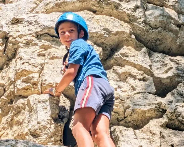 Enfant souriant escaladant un rocher avec un casque bleu.