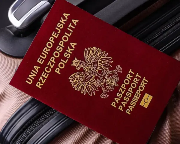 Czerwony paszport Polski z godłem orła leży na brązowej walizce.
