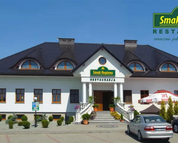 Restauracja "Smak Regionu" z białym budynkiem, schodami i samochodami na parkingu.
