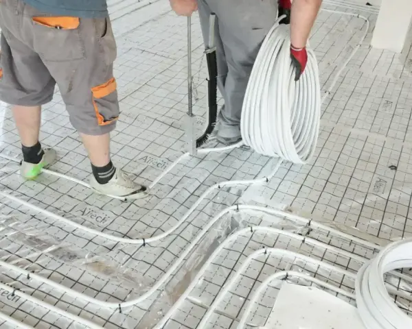 Pracownicy układają rury do ogrzewania podłogowego na siatce. Wkrótce powstanie tu szlichta, która zapewni komfort cieplny.