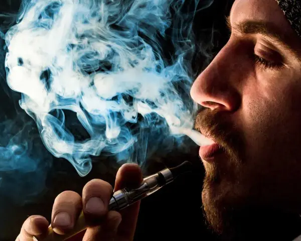 Hombre vapeando, el vaper sin nicotina es malo. El humo azul forma figuras fantasmagóricas.