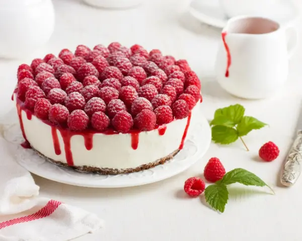 Himbeertorte mit Mascarpone, üppig belegt mit frischen Himbeeren und rotem Fruchtsirup, der über den Rand tropft.