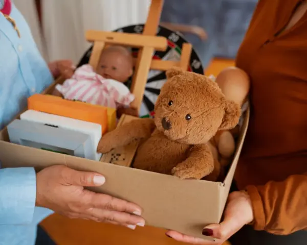 Pudełko z zabawkami: miś, lalka, domino i ramki. Szukasz, gdzie oddać zabawki Warszawa?