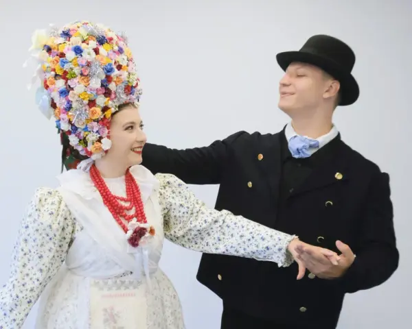 Para tańczy w strojach ludowych, co to folklor. Ona ma bogato zdobiony kwiatami wianek, on czarny kapelusz i marynarkę.
