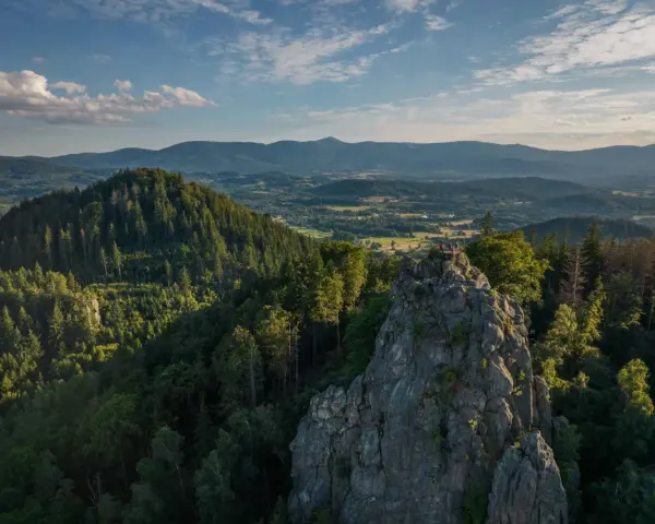 Widok na skalne formacje Rudawy Janowickie, porośnięte lasem, z ludźmi na szczycie. W tle rozległa panorama gór i dolin.