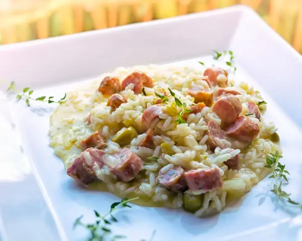 Un cremoso risotto con salsiccia, piselli e timo, servito su un piatto bianco.