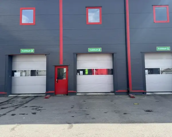 Grå fasad med röda detaljer och tre portar märkta Tvätthall 1, 2 och 3. En röd dörr finns mellan portarna.