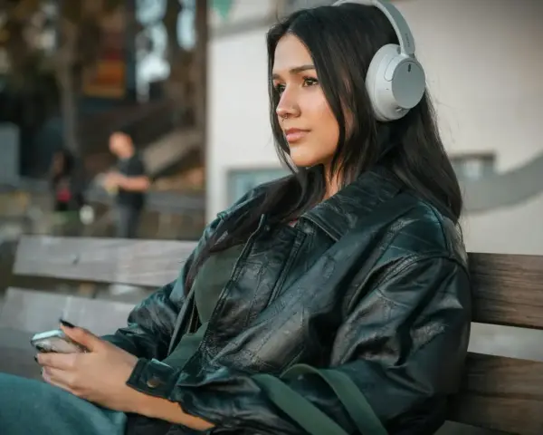 Młoda kobieta w słuchawkach, słuchająca podcastu o wymowie francuskiej, siedzi na ławce, trzymając telefon.