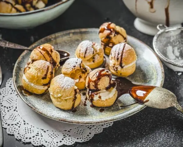 Köstliche Profiteroles, bestäubt mit Puderzucker und beträufelt mit Schokoladensauce. Ein wahrer Genuss, wie beim original profiteroles rezept.
