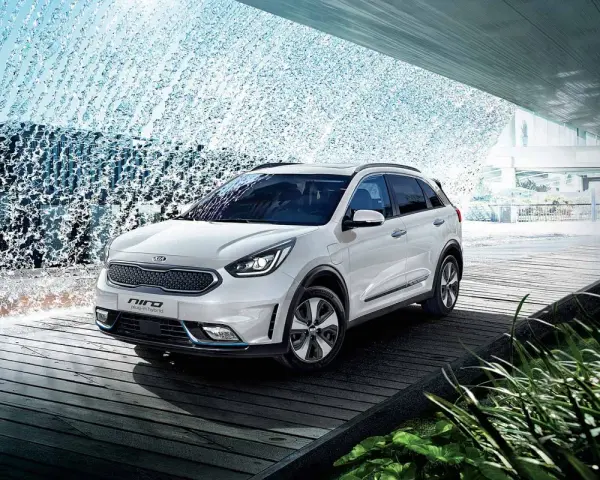 Biały Kia Niro Plug-in Hybrid na drewnianej platformie, otoczony wodnymi kaskadami i zielenią.