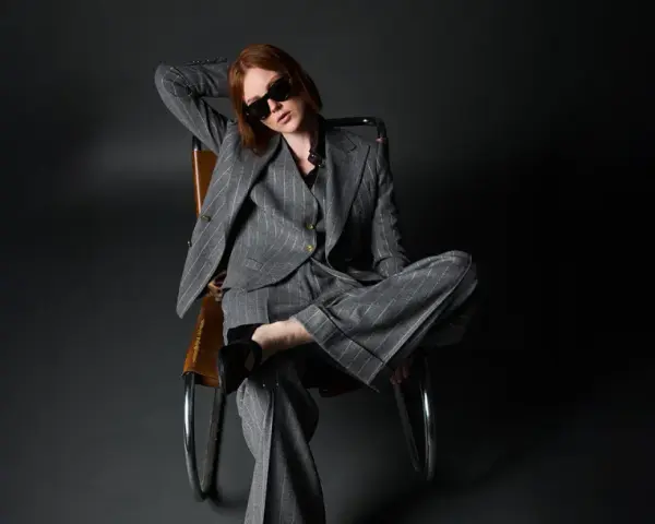 Donna con outfit giacca doppiopetto donna a righe grigie, occhiali da sole, seduta su una poltrona di pelle.