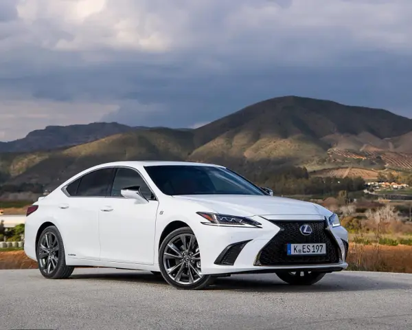 Biały Lexus ES 300h zaparkowany na tle górskiego krajobrazu. Elegancki sedan prezentuje się okazale na tle natury.