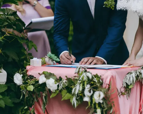 Pan młody podpisuje dokumenty, a obok stoi panna młoda. Zastanawiasz się, ile kosztuje ślub cywilny?