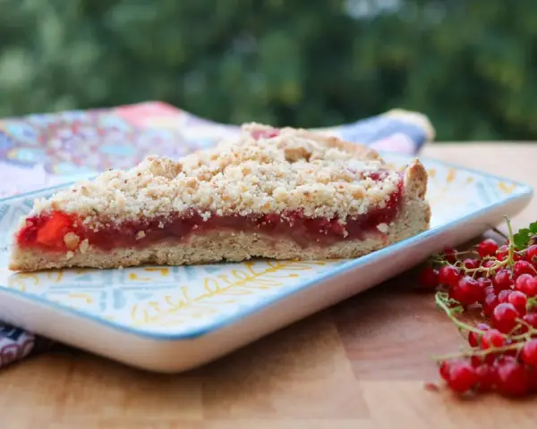 Ein Stück saftiger Johannisbeer Streuselkuchen mit frischen roten Johannisbeeren daneben.