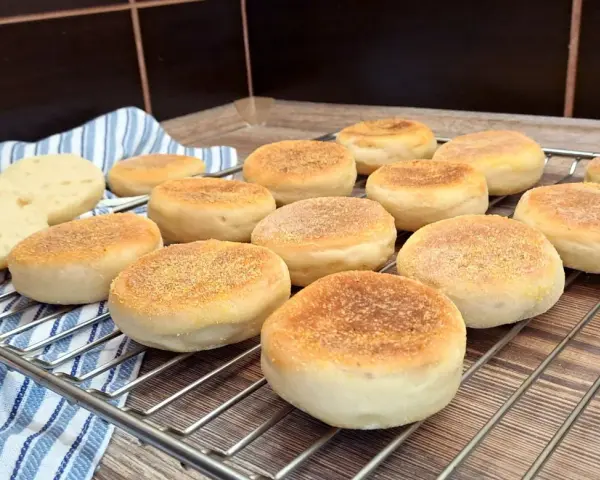 Świeżo upieczone muffiny angielskie, lekko zrumienione, czekają na śniadanie. Dwa przekrojone bułeczki odsłaniają puszyste wnętrze.