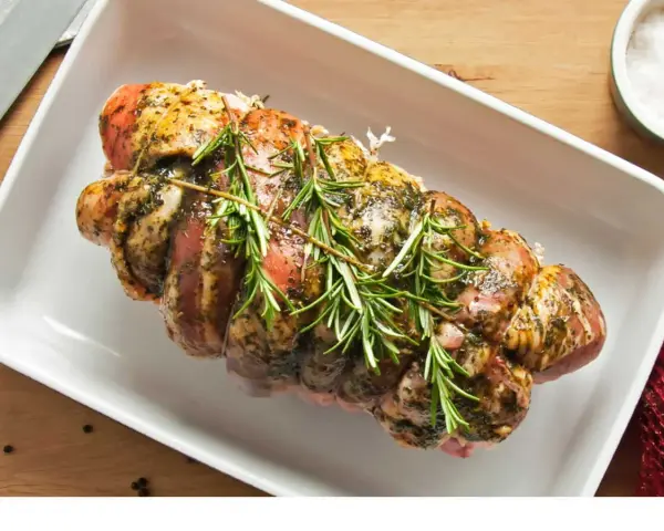 Rôti de porc Orloff, assaisonné et garni de romarin frais, prêt à être cuit dans un plat blanc.