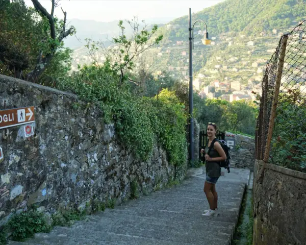 Una ragazza con zaino su un sentiero panoramico, con un cartello che indica Camogli. Perfetto per chi cerca dove dormire sul Cammino del Tigullio.
