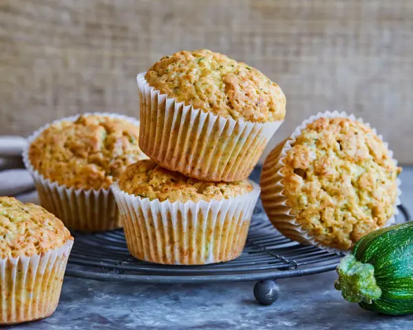 Saftige zucchini-muffins auf einem Gitter, daneben eine frische Zucchini.