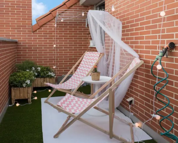 Acogedora terraza de 10 metros cuadrados con dos tumbonas, plantas y luces decorativas. Ideal para relajarse.