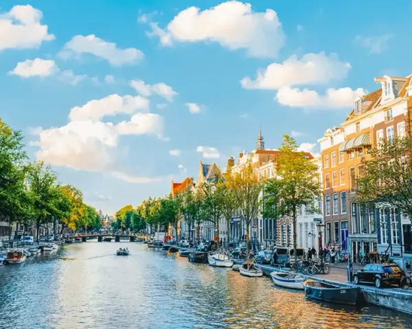 Widok na kanał w Amsterdamie, z łodziami, kamienicami i zielenią. Idealne miejsce na spacer, gdzie jest Amsterdam.