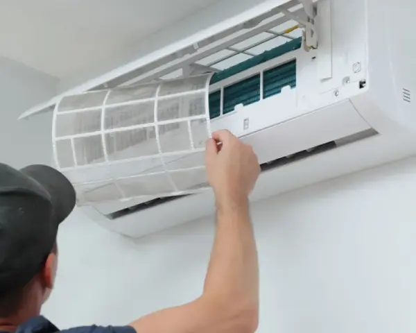 Un homme retire un filtre à air sale d'une unité de climatisation murale, étape essentielle de l'entretien climatisation maison pour un air sain.