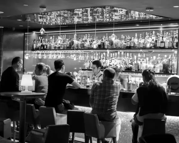 Gente en un bar cine, con un camarero sirviendo bebidas detrás de la barra llena de botellas.