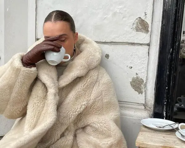 Vanilla girl w kremowym futrze pije kawę, otulona ciepłem i spokojem.
