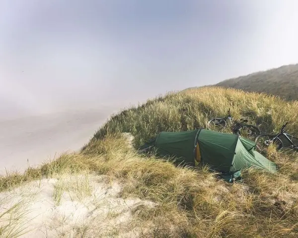 Grön tält och cyklar på en gräsbevuxen sanddyn vid havet. En idyllisk plats för äventyr i sanddynerna Danmark.