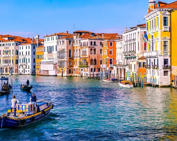 Venezia: turisti in gondola e vaporetti sul Canal Grande, tra palazzi colorati e acque azzurre.