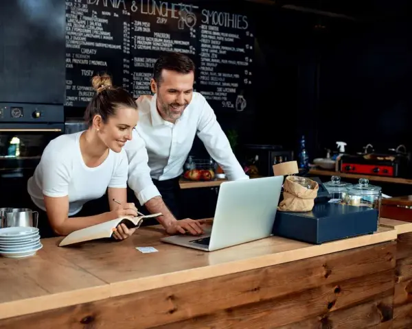 Pareja revisa menú en laptop, planificando su negocio de hostelería en España.