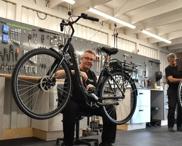 Mekaniker arbetar med en elcykel i verkstad. Verktyg på väggen visar att detta är en plats för bidrag till elcykel.