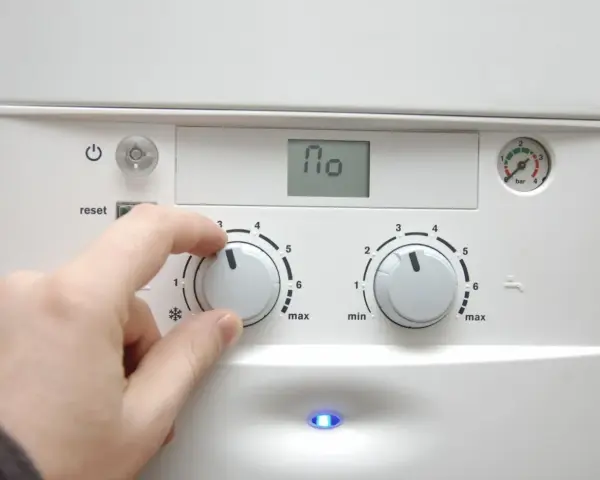 Dłoń reguluje pokrętłem pieca, przygotowując dom na nadchodzący sezon grzewczy. Na wyświetlaczu widnieje "110".