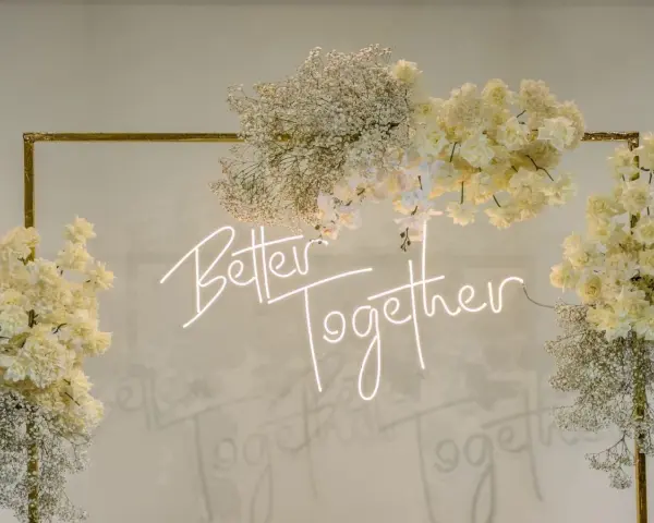 Elegancka ściana z kwiatów w kremowych odcieniach, ozdobiona neonowym napisem "Better Together".