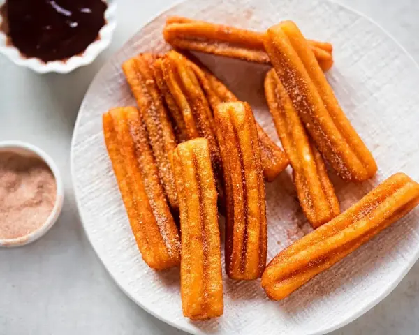 Churros sin gluten espolvoreados con azúcar y canela, servidos con chocolate caliente.