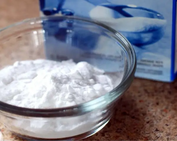 Una ciotola di vetro piena di polvere bianca, probabilmente bicarbonato di potassio, accanto a una scatola blu sfocata.
