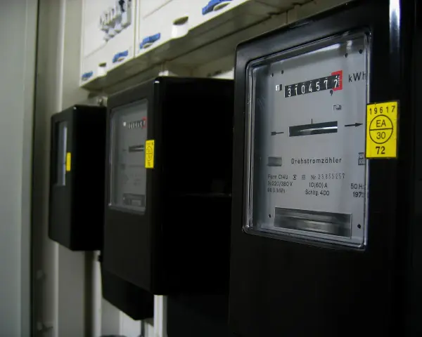 Szereg liczników energii elektrycznej, każdy z wyświetlaczem pokazującym zużycie. Jeden z nich ma żółtą naklejkę z napisem "silnik inwerterowy".