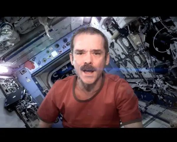 Chris Hadfield singt "Space Oddity" in der ISS. Sein Gesicht mit Schnurrbart ist im Vordergrund, der Raumschiff-Innenraum im Hintergrund.