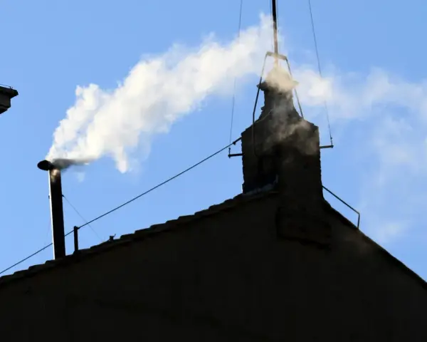 Biały dym z komina, jak sygnał wyboru nowego papieża, unosi się na tle błękitnego nieba.