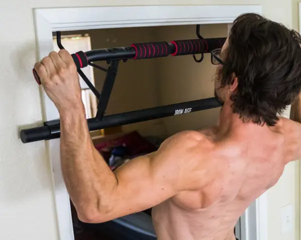 Homme musclé s'entraînant avec une barre de tirage porte d'entrée. Avis : installation facile et solide pour un entraînement efficace.