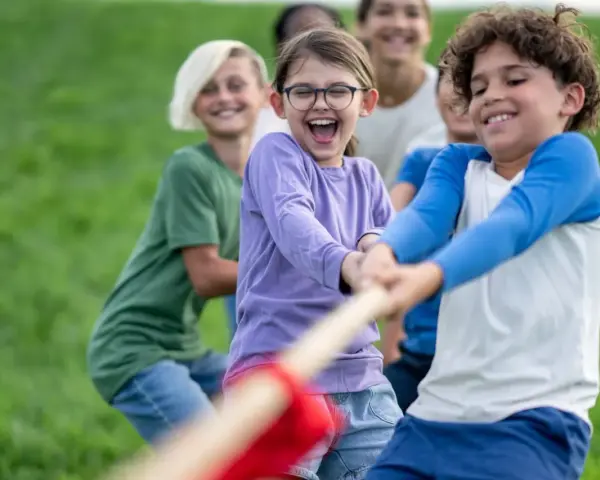 Des enfants joyeux jouent à la corde dans un champ d'herbe verte.