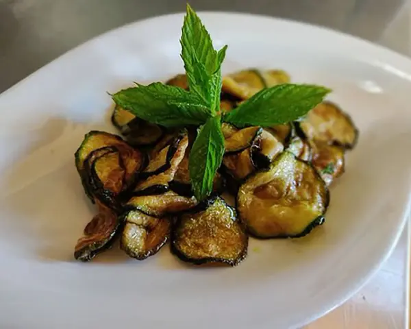 Zucchine alla scapece dorate e croccanti, guarnite con foglie di menta fresca, servite su un piatto bianco.