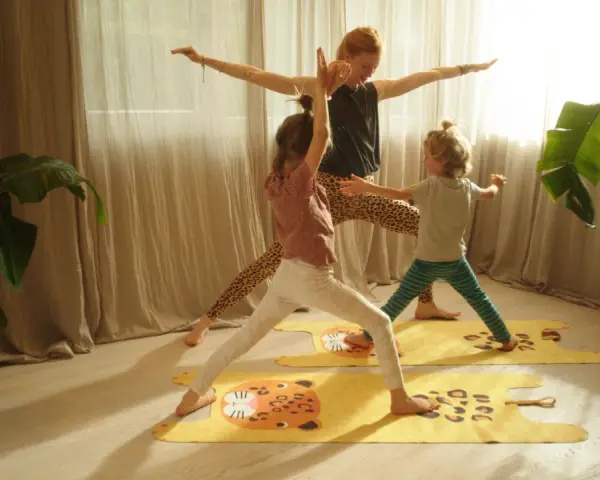 Eine Frau und zwei Kinder üben Yoga auf bunten Matten. Die Kinder haben Spaß bei den Yoga-Übungen.