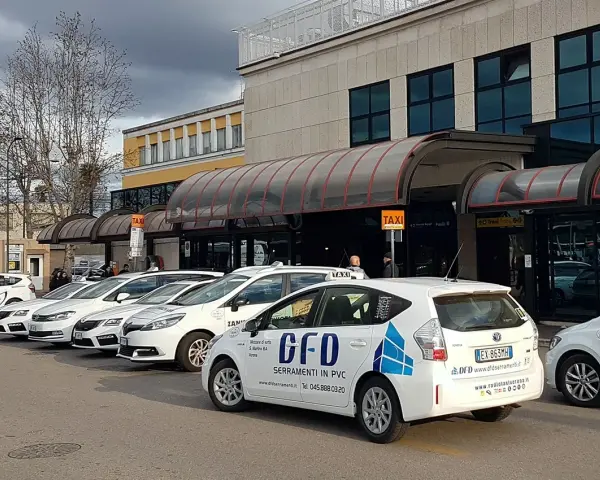 Reihe weißer Taxis vor einem Gebäude mit Taxischildern.