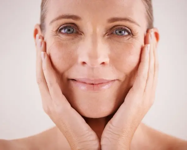 Visage d'une femme aux mains sur les joues, montrant les signes du temps et les défis des problèmes de peau et ménopause.